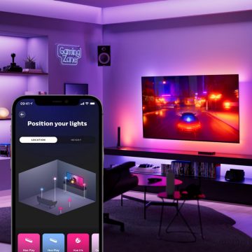 Hue sync app's virtual room set-up screen on mobile device in the foreground. Racing game on hanging TV screen and synced-up lighting in the background.